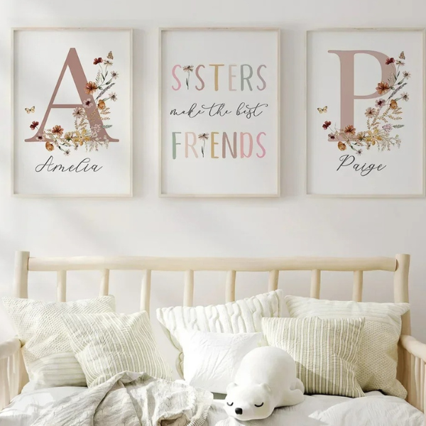 Décoration murale avec triptyque fleuri pour sœurs, affiches encadrées en bois clair au-dessus d’un lit d’enfant dans une chambre aux tons neutres et chaleureux.