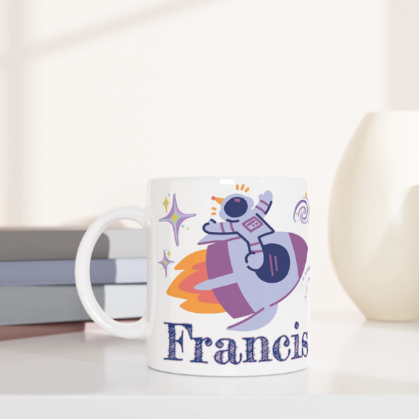 Mug personnalisé tout blanc avec illustration d’un astronaute sur une fusée dans l’espace, parfait pour un cadeau enfant original.