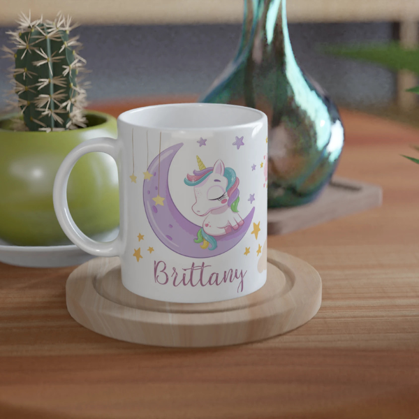 Mug personnalisé tout blanc avec licorne endormie sur un croissant de lune et arc-en-ciel, idéal pour un cadeau féerique et apaisant.