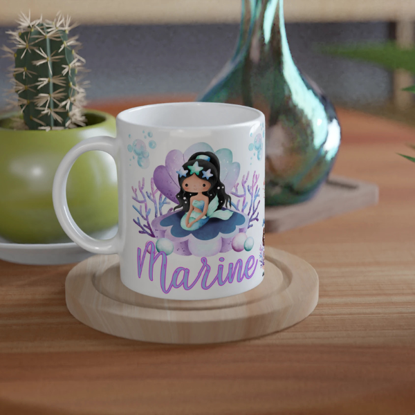 Mug personnalisé tout blanc avec illustration de sirène assise sur un coquillage magique, coraux et décor marin, idéal comme cadeau enfant.