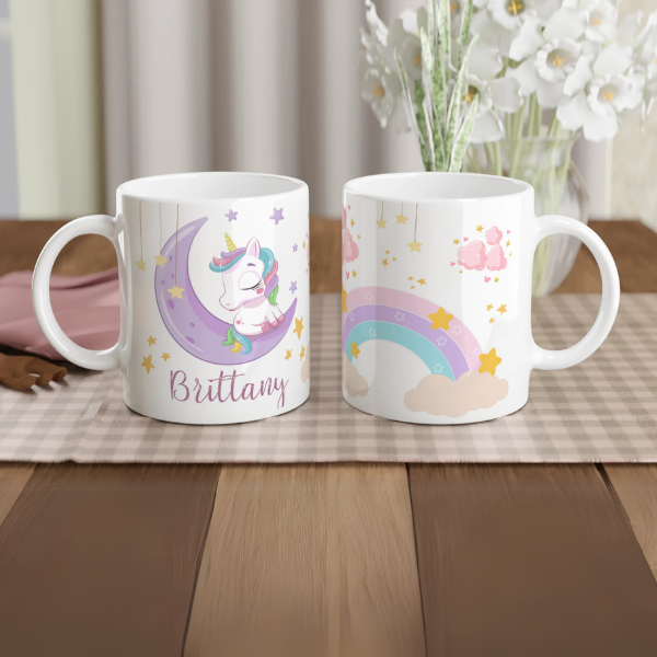 Mug personnalisé tout blanc avec licorne endormie sur un croissant de lune et arc-en-ciel, idéal pour un cadeau féerique et apaisant.