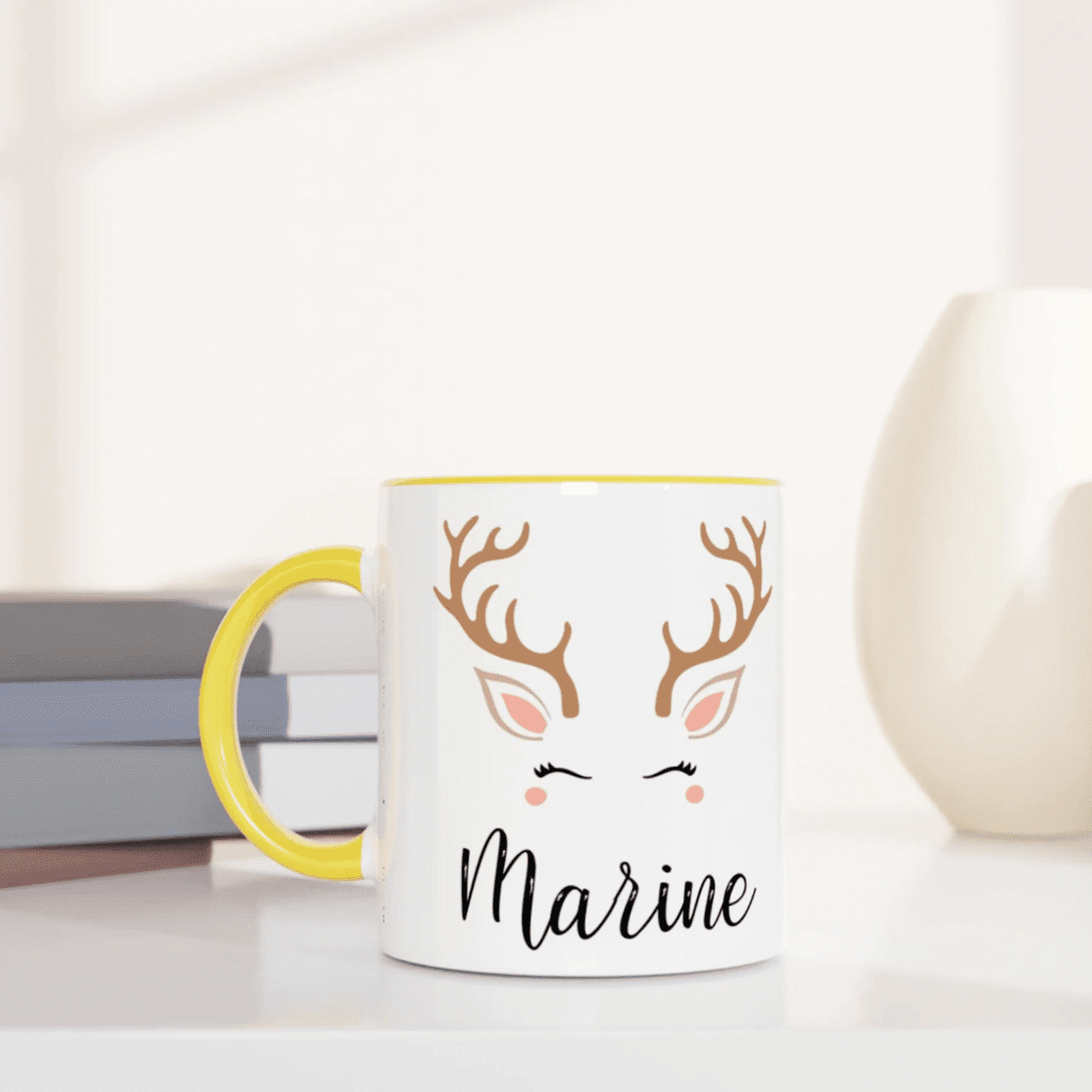 Mug blanc de Noël avec illustration de renne minimaliste, joues rosées et bois élégants, anse jaune et intérieur jaune.