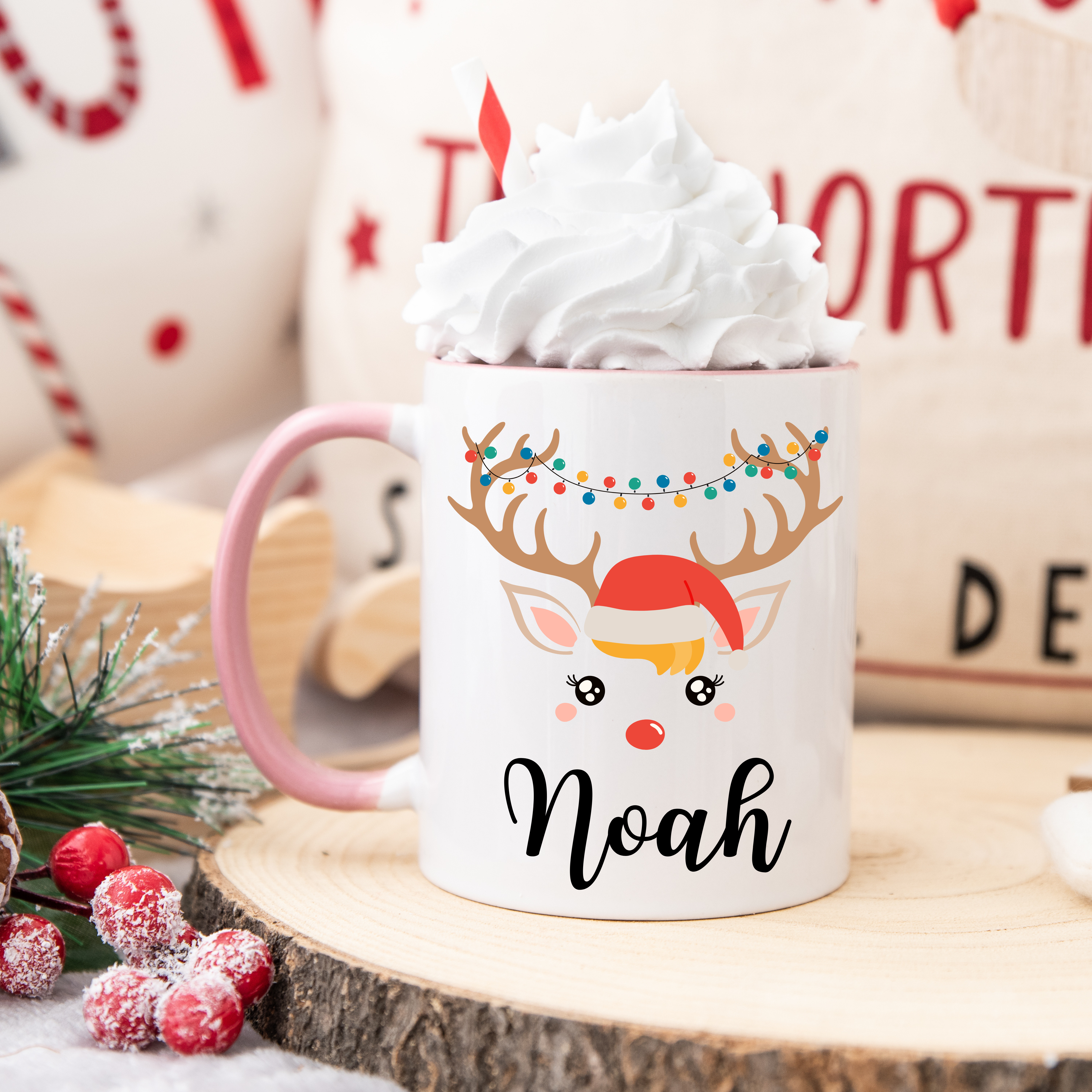 Mug de Noël illustré d’un renne festif avec bonnet rouge et guirlande lumineuse, anse rose et intérieur rose.