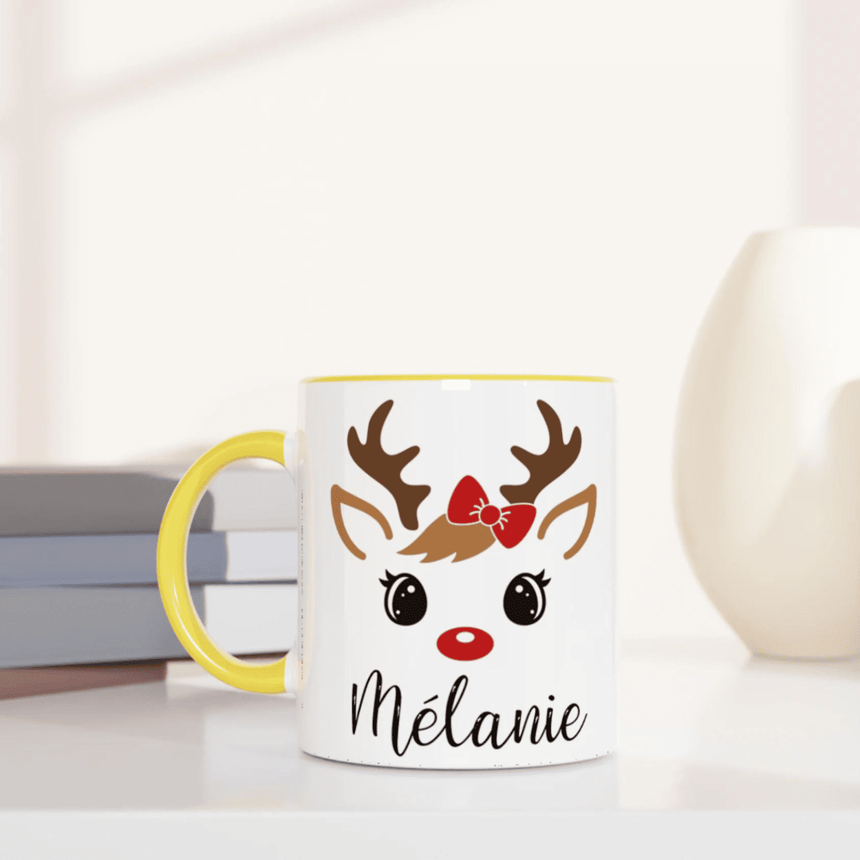 Mug de Noël avec illustration de renne aux yeux ouverts et nœud rouge, anse jaune et intérieur jaune.