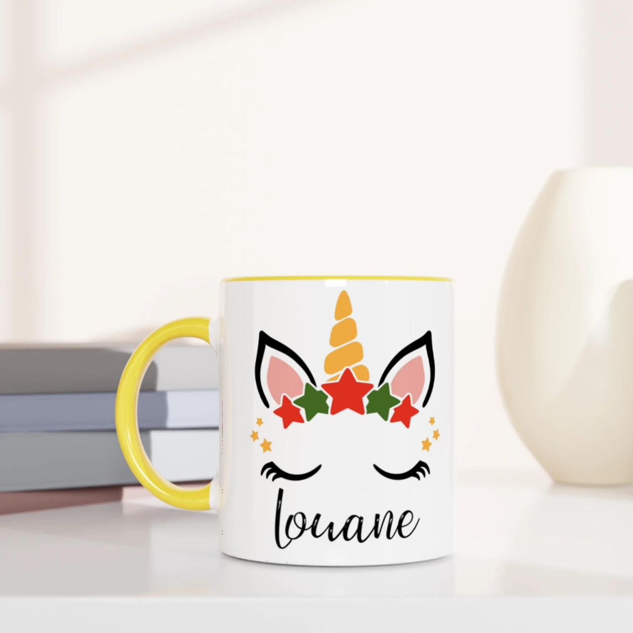 Mug licorne de Noël avec corne dorée et couronne d’étoiles rouges et vertes, anse jaune et intérieur jaune.