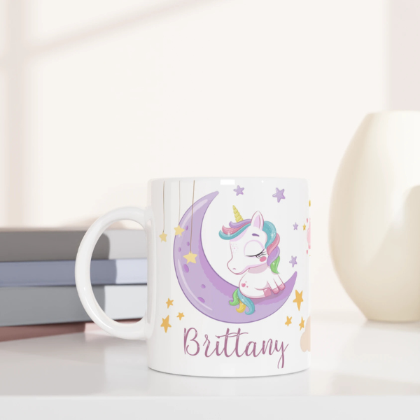 Mug personnalisé tout blanc avec licorne endormie sur un croissant de lune et arc-en-ciel, idéal pour un cadeau féerique et apaisant.