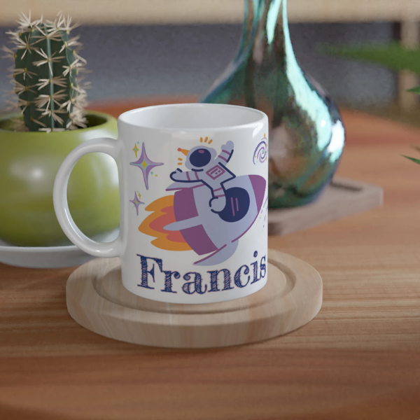 Mug personnalisé tout blanc avec illustration d’un astronaute sur une fusée dans l’espace, parfait pour un cadeau enfant original.