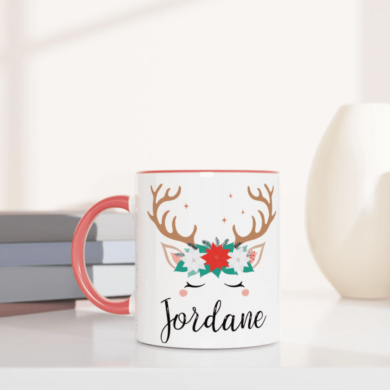 Mug de Noël avec motif renne et couronne florale, anse rose et intérieur rose, posé sur une table avec chantilly et décoration festive.