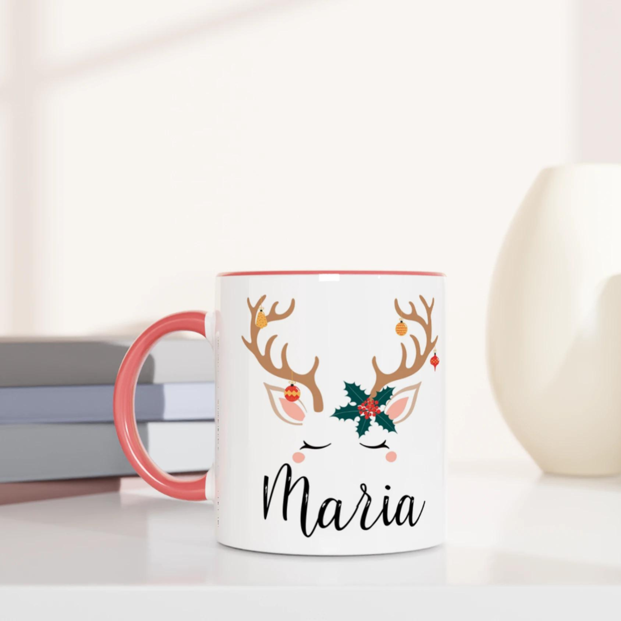 Mug de Noël décoré d’un renne aux bois ornés de décorations et feuille de houx, anse rose et intérieur rose.
