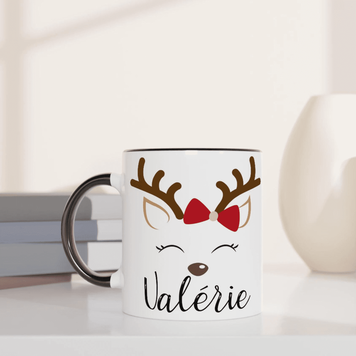 Mug de Noël blanc avec illustration de renne aux yeux fermés et nœud rouge, anse noire et intérieur noir.