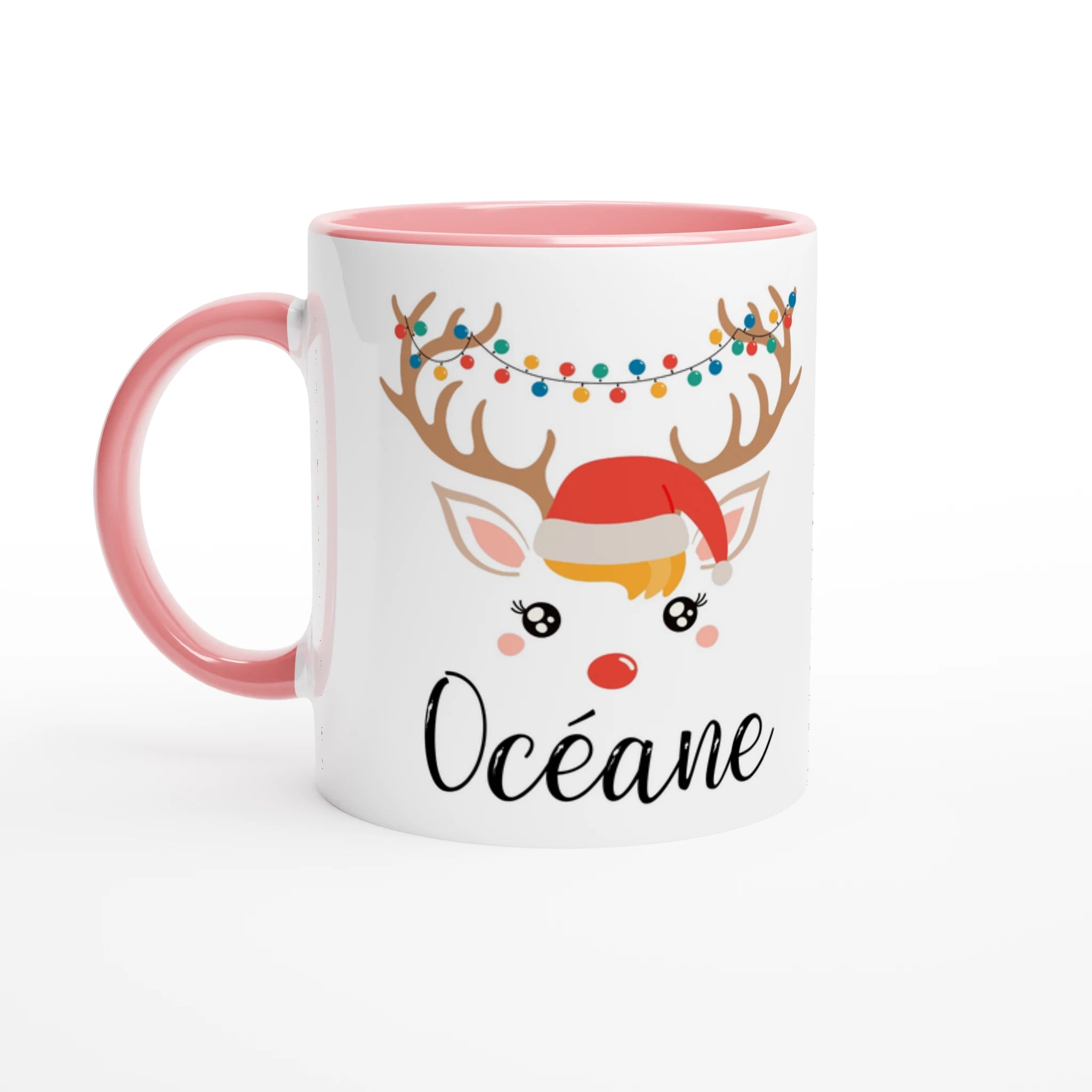 Mug de Noël illustré d’un renne festif avec bonnet rouge et guirlande lumineuse, anse rose et intérieur rose.