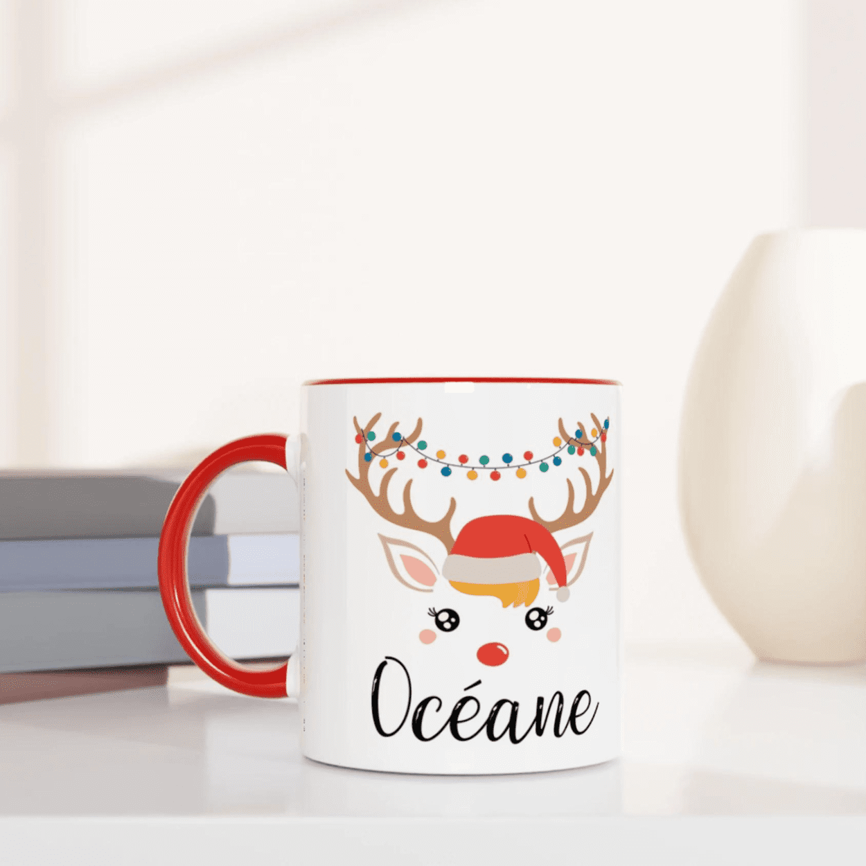 Mug de Noël décoré d’un renne avec bonnet rouge et guirlande lumineuse colorée, anse rouge et intérieur rouge.