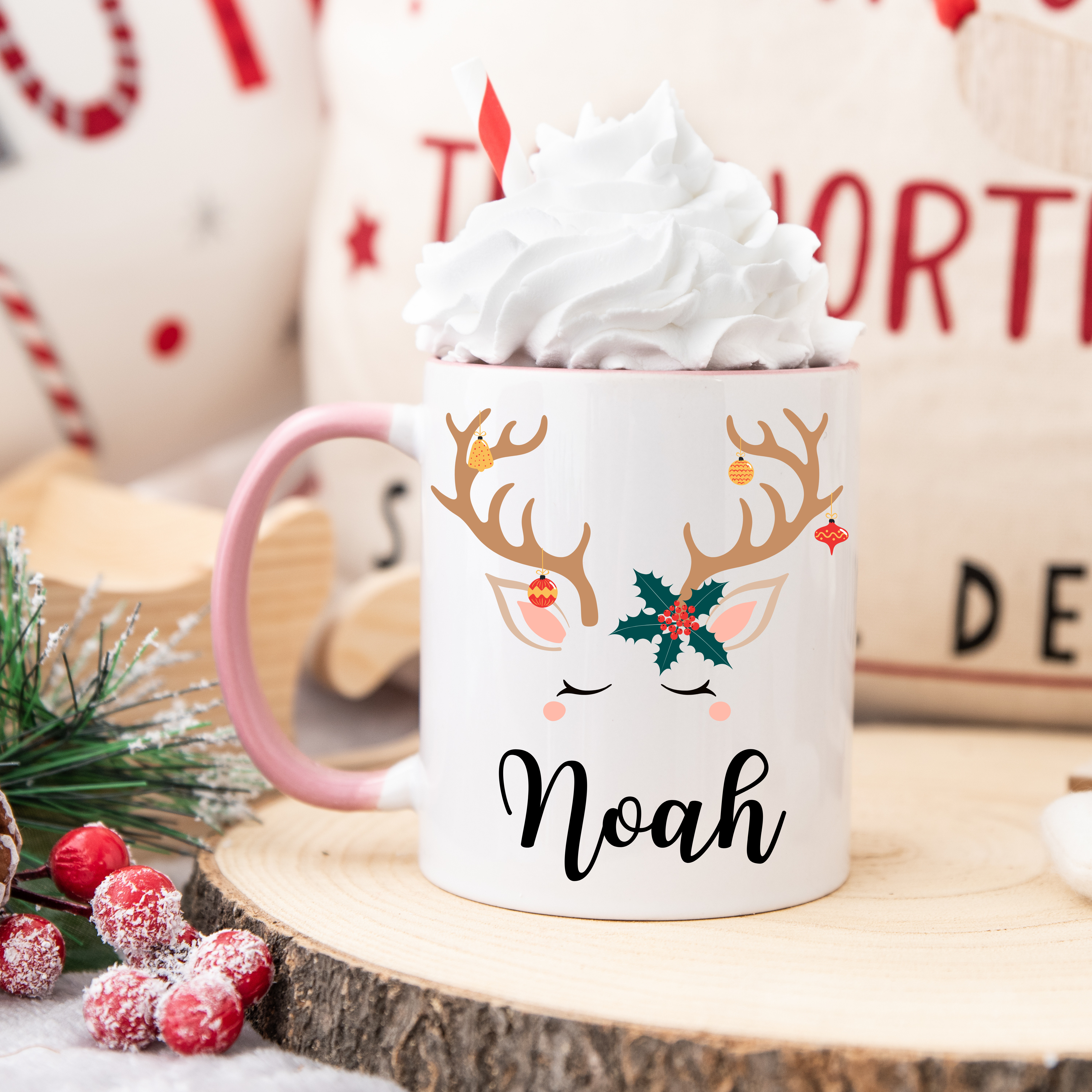 Mug de Noël décoré d’un renne aux bois ornés de décorations et feuille de houx, anse rose et intérieur rose.