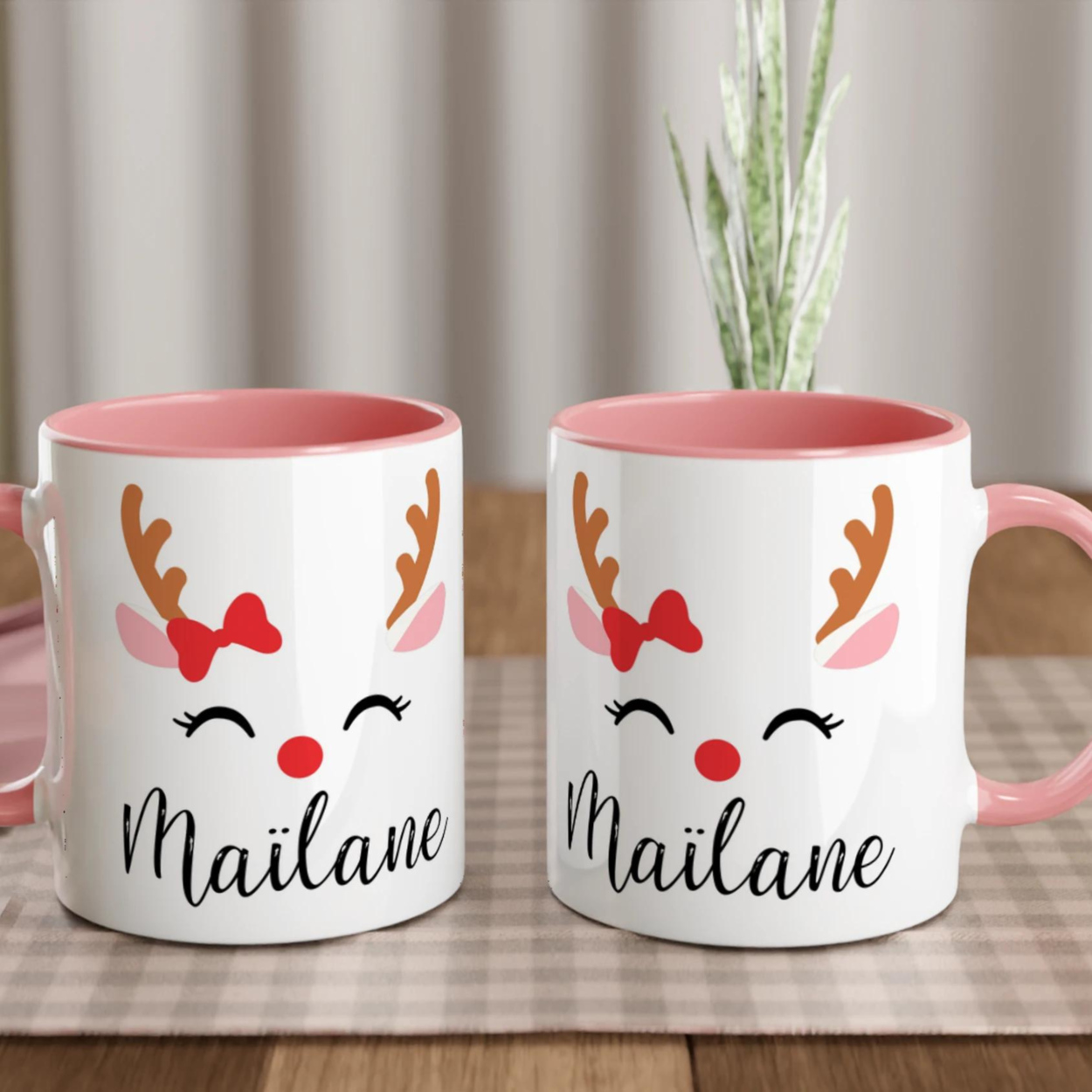 Mug de Noël décoré d’un renne festif avec nœud rouge et bois stylisés, anse rose et intérieur rose.