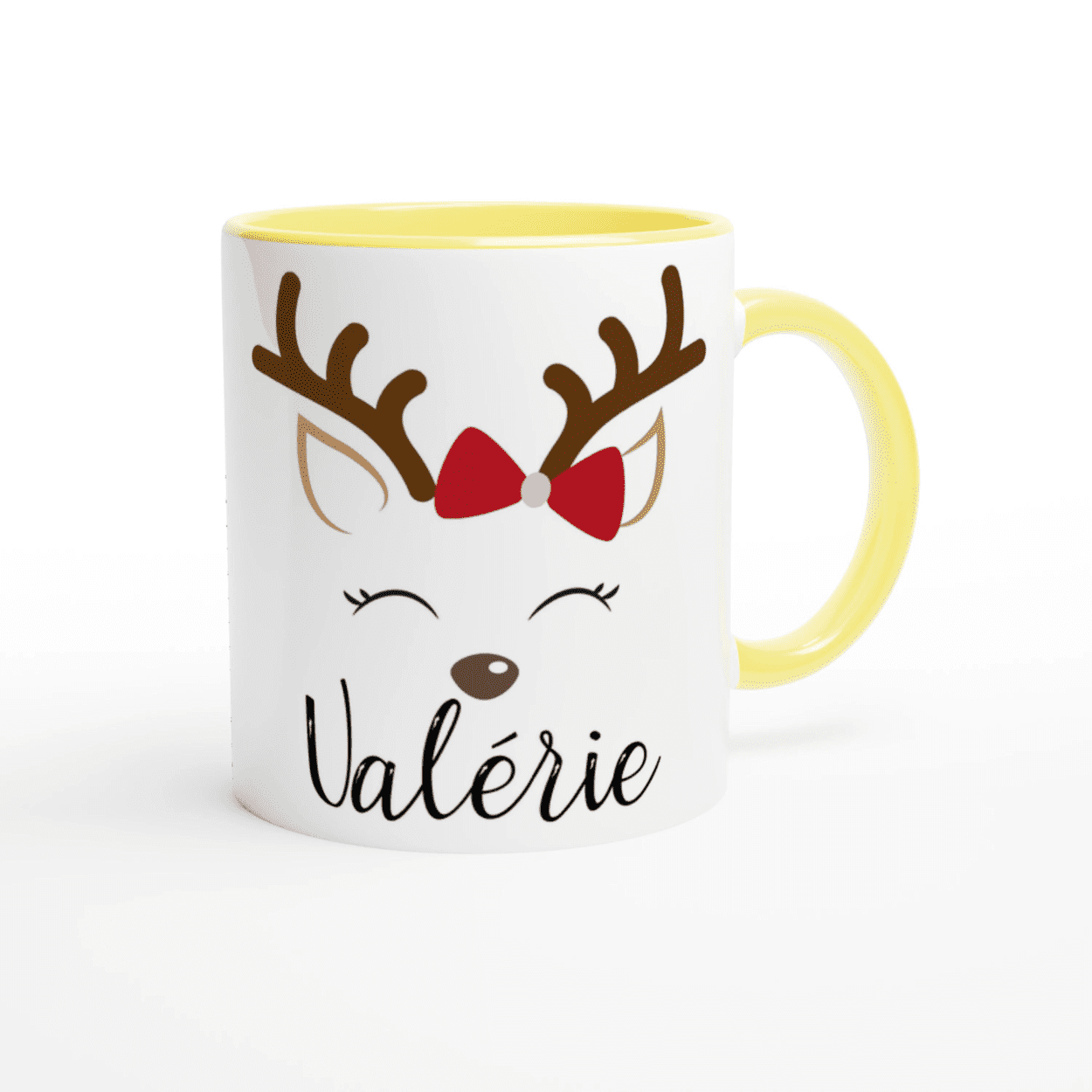 Mug blanc de Noël avec motif renne aux yeux fermés et nœud rouge, anse jaune et intérieur jaune.