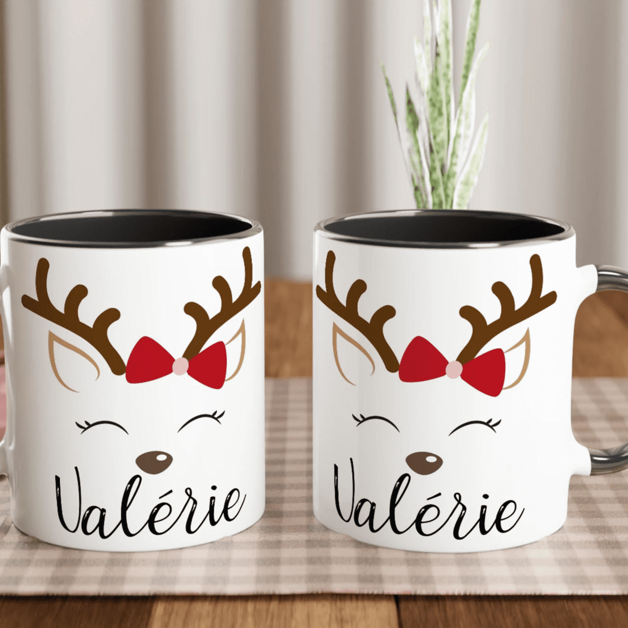 Mug de Noël blanc avec illustration de renne aux yeux fermés et nœud rouge, anse noire et intérieur noir.