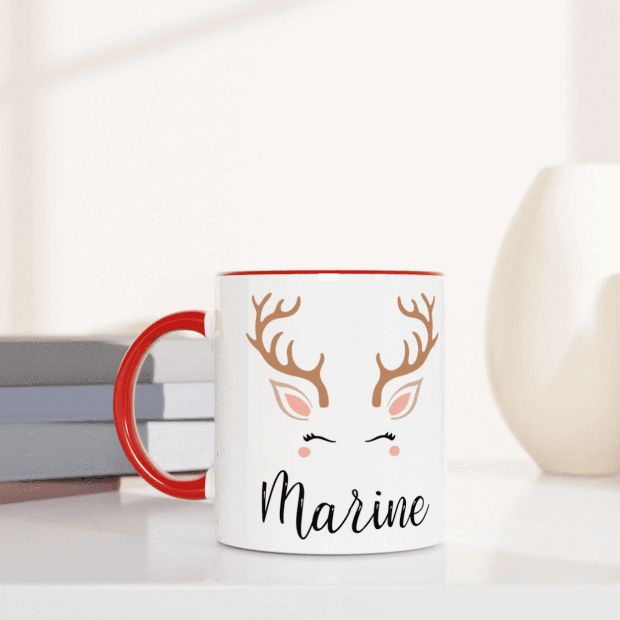 Mug de Noël décoré d’un renne stylisé aux yeux fermés, design épuré, anse rouge et intérieur rouge.