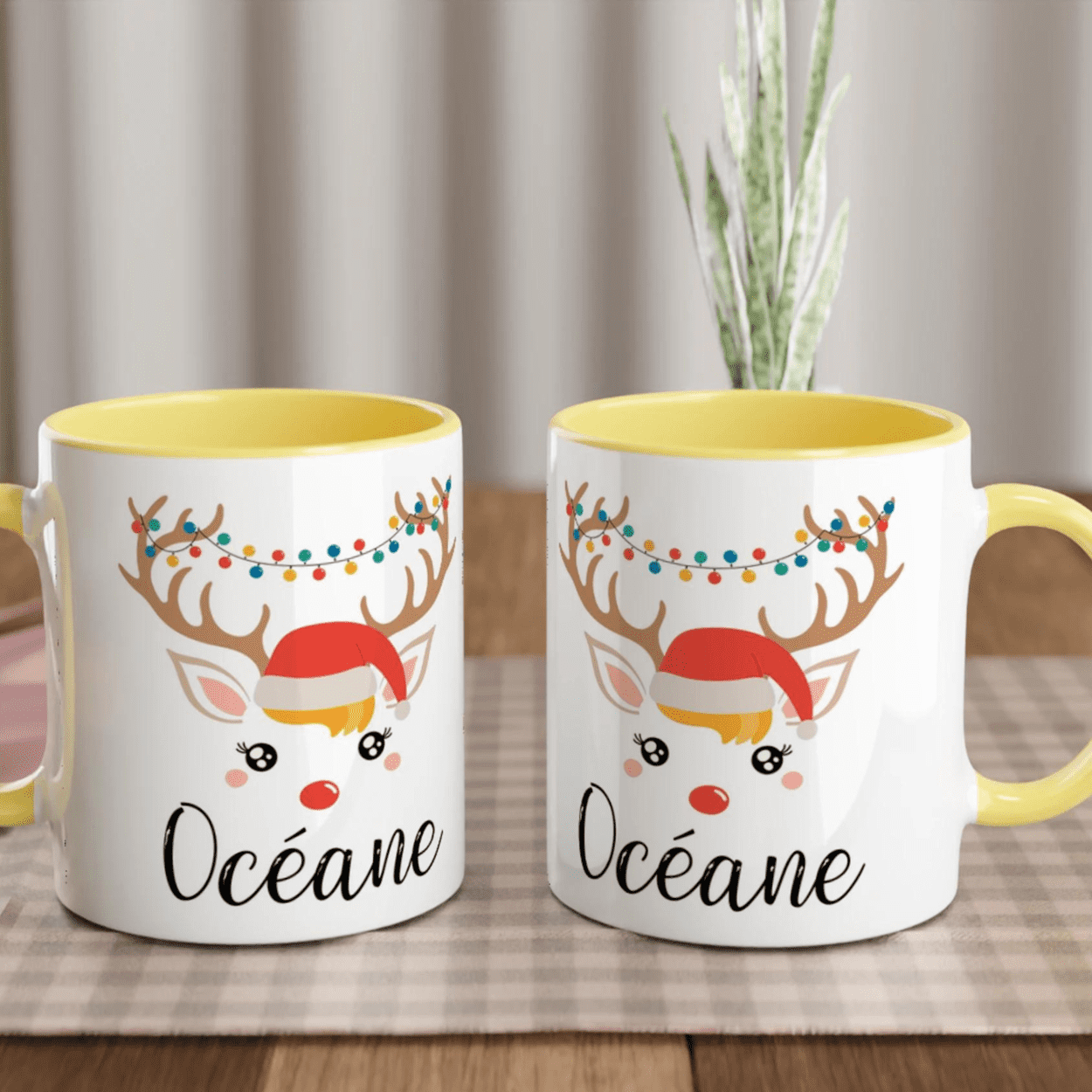 Mug de Noël avec illustration de renne portant un bonnet et une guirlande lumineuse, anse jaune et intérieur jaune.