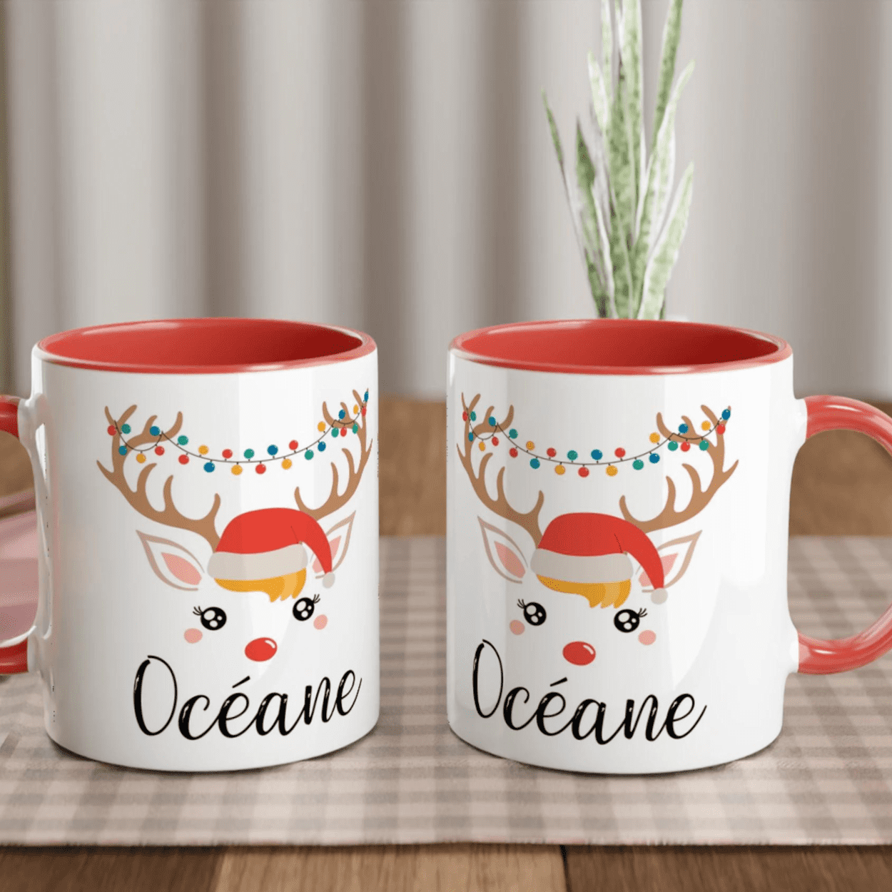 Mug de Noël décoré d’un renne avec bonnet rouge et guirlande lumineuse colorée, anse rouge et intérieur rouge.
