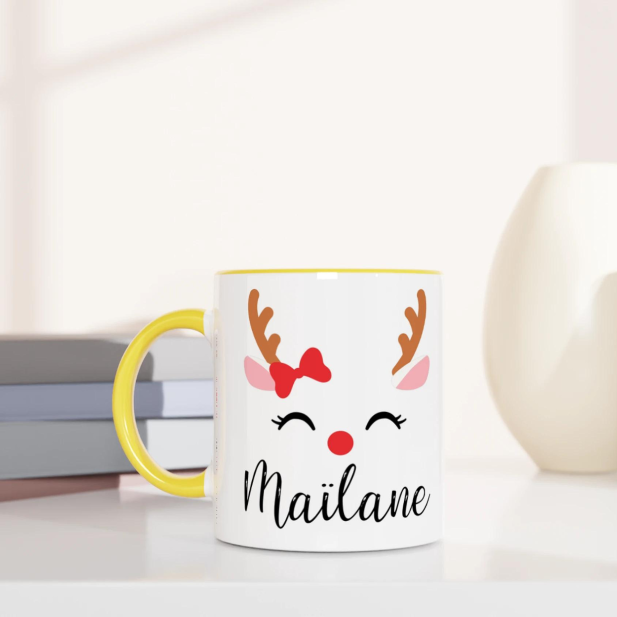 Mug de Noël avec motif renne aux yeux fermés et nœud rouge, anse jaune et intérieur jaune.