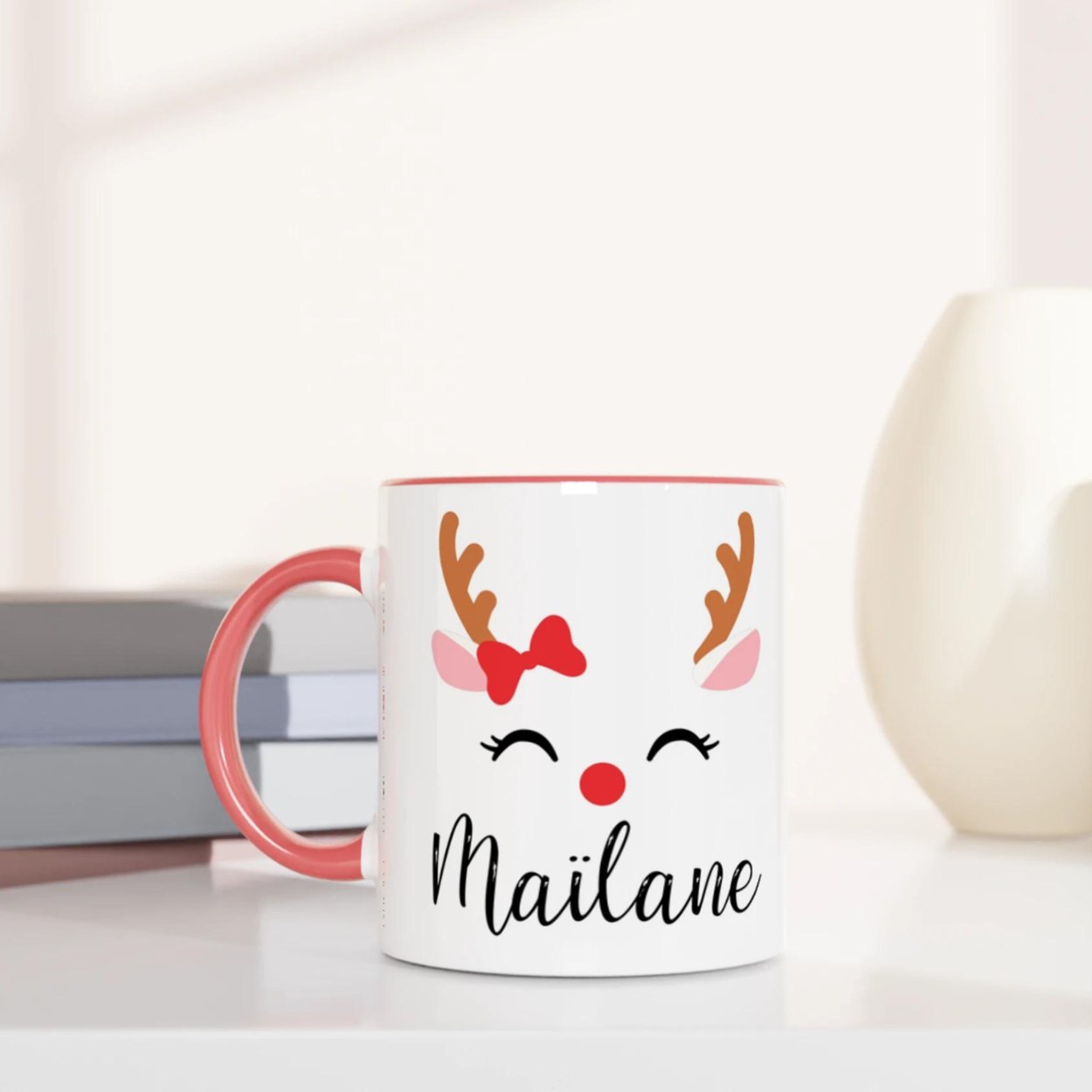 Mug de Noël décoré d’un renne festif avec nœud rouge et bois stylisés, anse rose et intérieur rose.