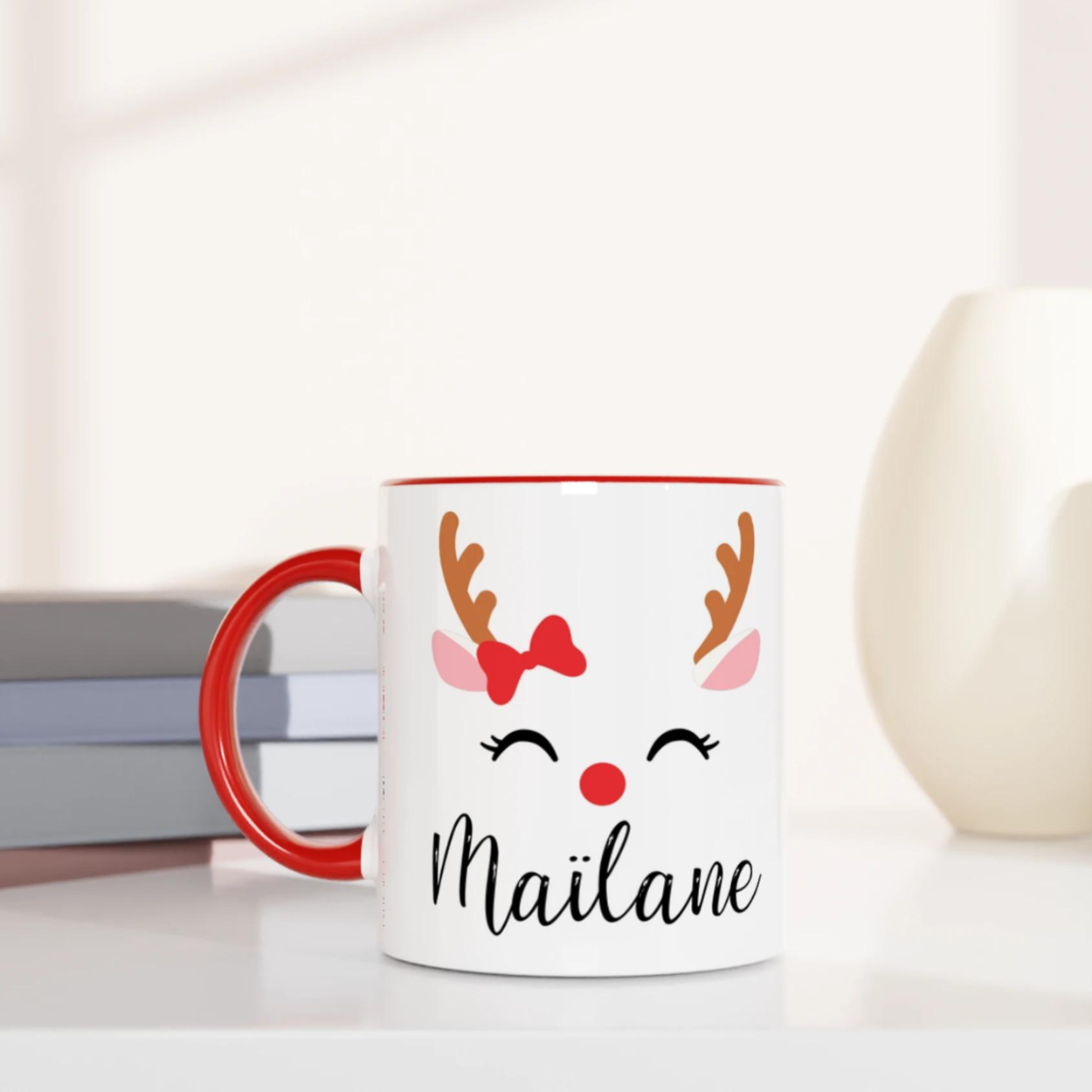 Mug de Noël illustré d’un renne avec nœud rouge et nez rouge, anse rouge et intérieur rouge.